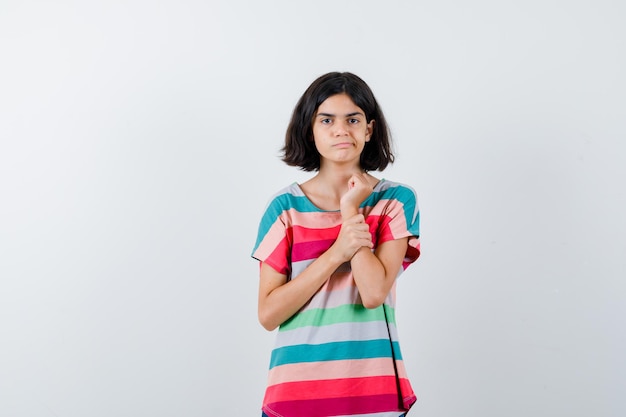 Foto grátis jovem colocando a mão no antebraço em uma camiseta listrada colorida e olhando sério. vista frontal.