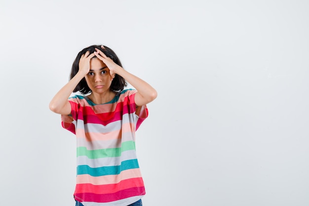 Jovem colocando as mãos na cabeça em uma camiseta listrada colorida e parecendo irritada, vista frontal.