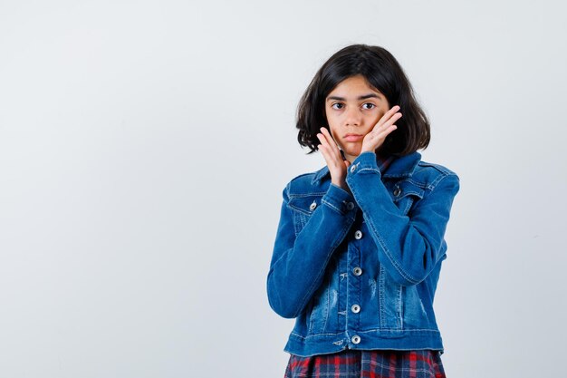 Jovem, colocando as mãos perto do rosto em camisa e jaqueta jeans e está linda. vista frontal.