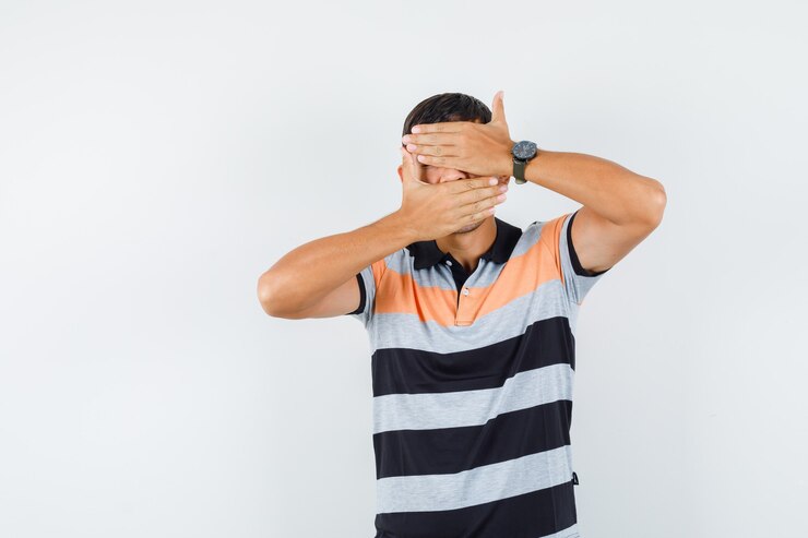 Foto grátis jovem com as mãos nos olhos e boca com uma camiseta e parecendo assustado
