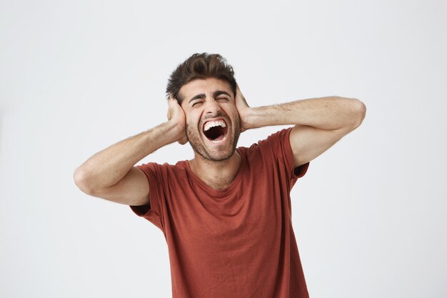 Foto grátis jovem com cabelo elegante, cobrindo os ouvidos e gritando. entrou em histeria por causa de discussões com a namorada ou os pais. não quero continuar ouvindo, abriu a boca em gritos expres