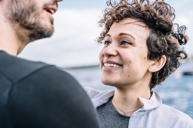 Foto grátis jovem com cabelo encaracolado e piercing no nariz, olhando para o parceiro com o mar fora de foco no