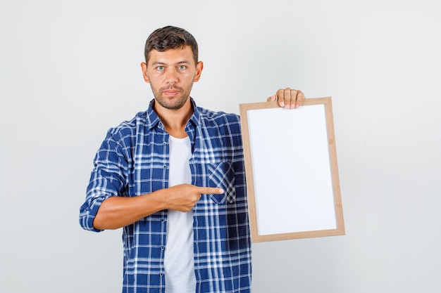 Jovem com camisa, apontando o dedo para o quadro branco e olhando sério, vista frontal.