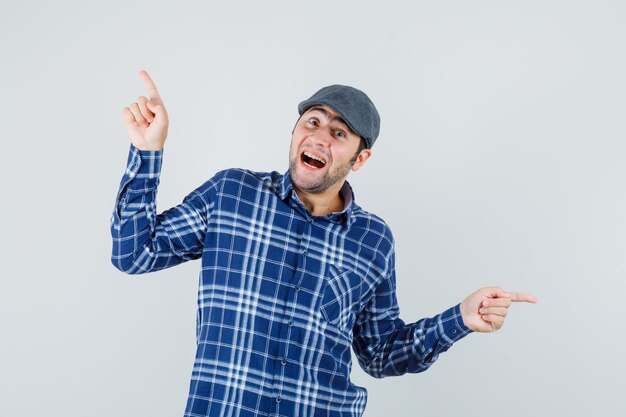 Jovem com camisa, boné apontando para longe e parecendo brincalhão, vista frontal.