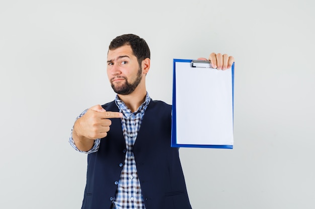 Foto grátis jovem com camisa, colete apontando para a área de transferência e olhando confiante, vista frontal.