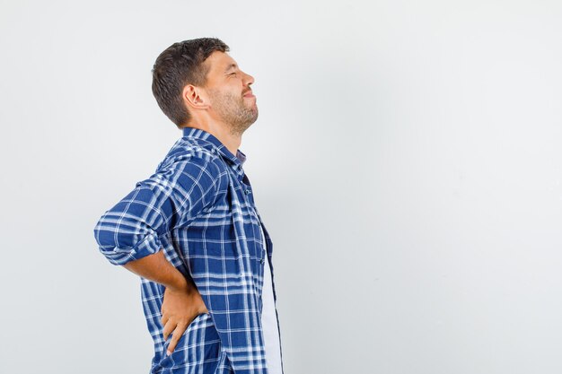 Jovem com camisa, sofrendo de dor nas costas e parecendo dolorido.