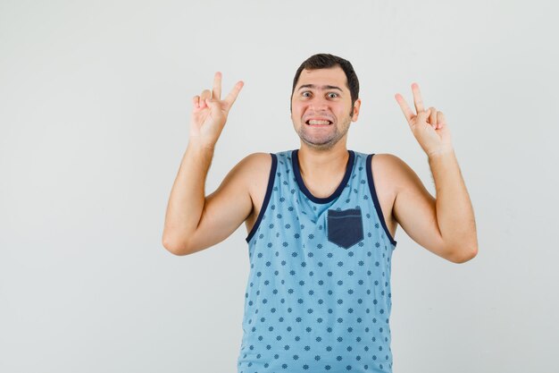 Jovem com camiseta azul mostrando gesto de vitória e parecendo feliz