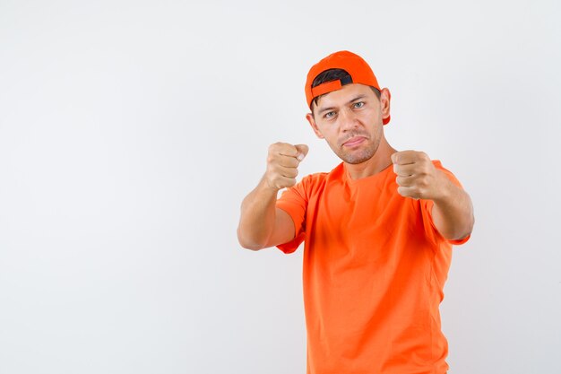 Jovem com camiseta laranja e boné em pose de boxeador e parecendo poderoso