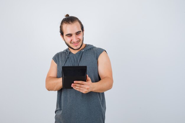 Jovem com capuz, contando com calculadora e olhando pensativo, vista frontal.