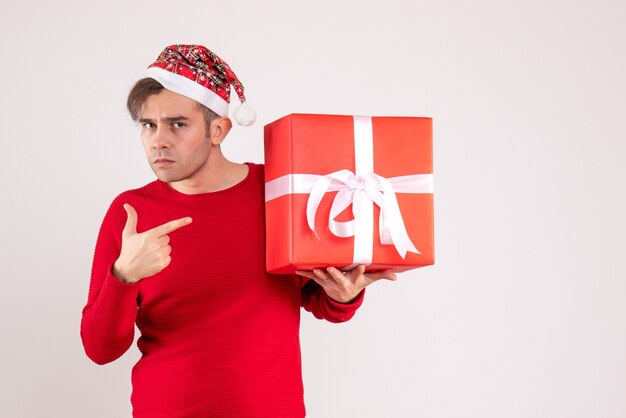 Jovem com chapéu de papai noel apontando para o presente de frente