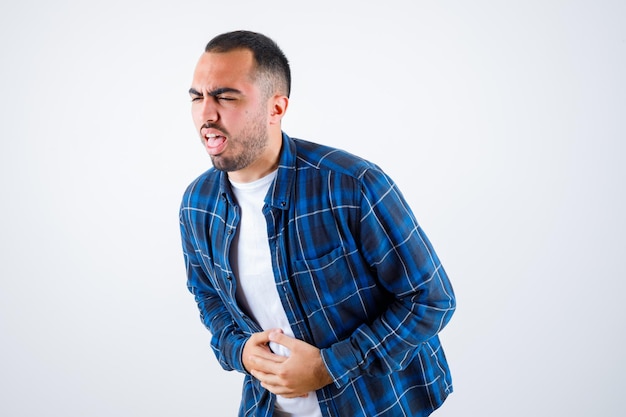 Foto grátis jovem com dor de barriga de camisa xadrez e camiseta branca e parecendo exausto