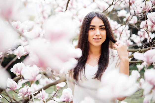 Jovem com flor de magnólia. Mulher jovem e bonita perto da árvore de flores da primavera.