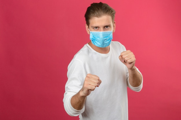 Foto grátis jovem com máscara de proteção médica socando o punho para lutar em pé sobre um fundo rosa isolado