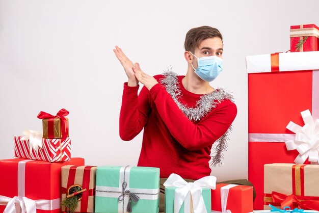 Jovem com máscara médica sentado ao redor dos presentes de Natal