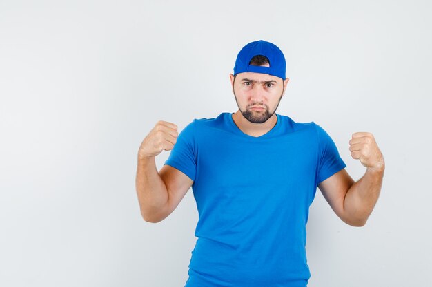 Jovem com os punhos erguidos cerrados na camiseta azul e boné e parecendo sério