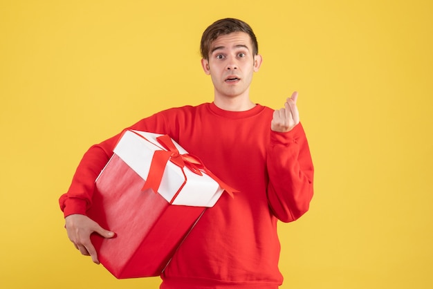 Jovem com suéter vermelho fazendo sinal de dinheiro em fundo amarelo de frente