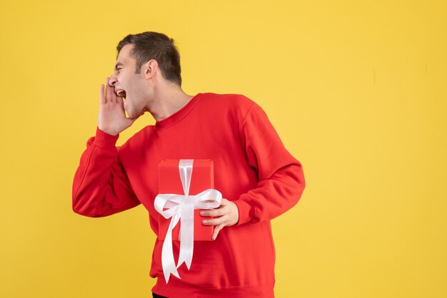 Jovem com suéter vermelho gritando sobre fundo amarelo