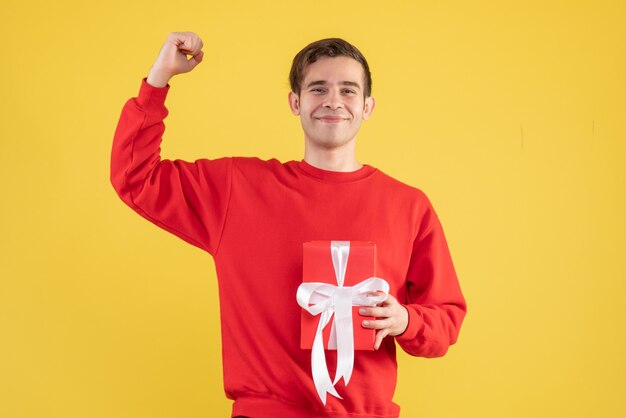 Jovem com suéter vermelho segurando um presente no local de cópia de fundo amarelo