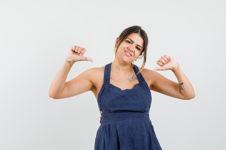 Foto grátis jovem com um vestido a apontar os polegares para si mesma e a parecer feliz