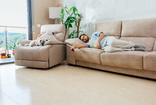 Jovem com uma aparência entediada e cansada segurando um controle remoto de TV e descansando em um sofá