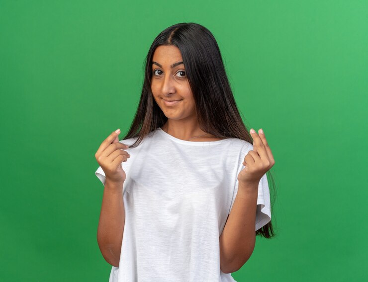 Foto grátis jovem com uma camiseta branca olhando para a câmera com um sorriso no rosto fazendo gesto de dinheiro esfregando os dedos