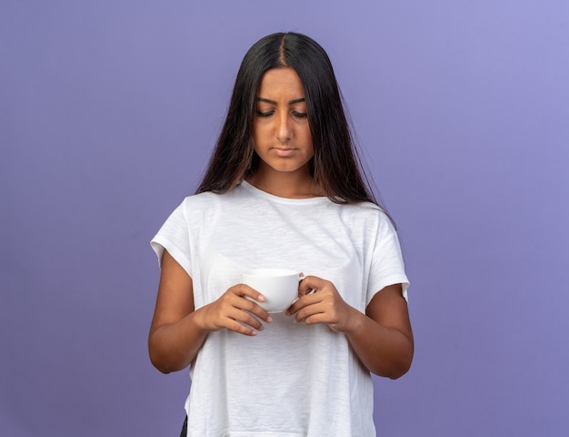 Jovem com uma camiseta branca segurando um copo olhando para ele com uma cara séria