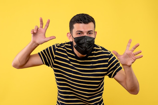 Jovem com uma camiseta listrada em preto e branco fazendo um gesto assustador de fundo amarelo