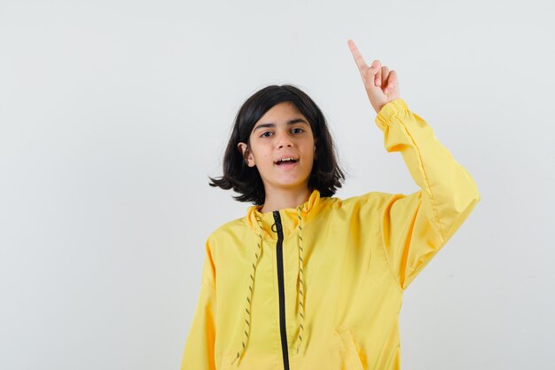 Jovem com uma jaqueta amarela levantando o dedo indicador num gesto de eureca e parecendo feliz