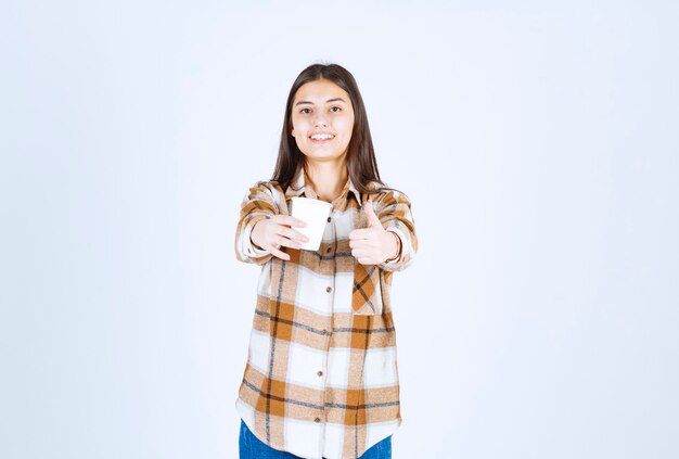 Foto grátis jovem com uma xícara de chá desistindo de polegares na parede branca.