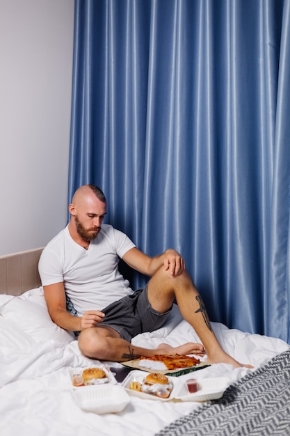 Foto grátis jovem comendo fast food em casa no quarto na cama