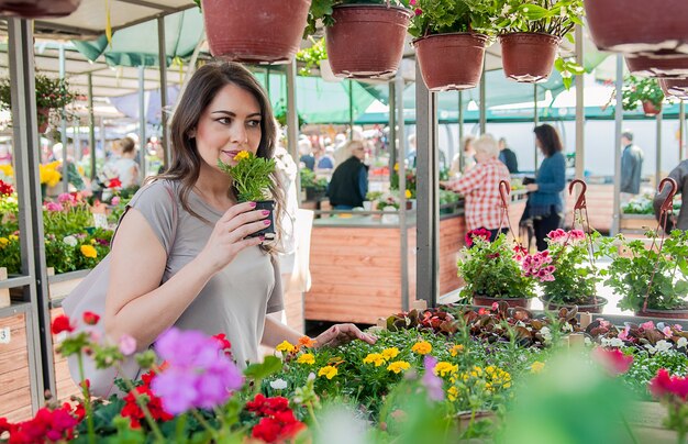 Jovem comprando flores em um centro de jardim. Minhas flores favoritas. Mulher olhando flores em uma loja. Retrato de uma mulher sorridente com flores em viveiro de plantas