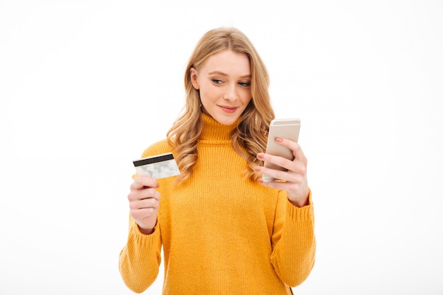 Jovem concentrada segurando o telefone móvel e cartão de crédito.