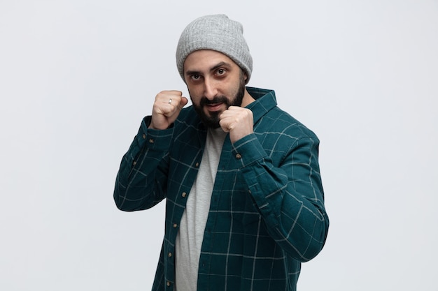 Foto grátis jovem confiante usando chapéu de inverno olhando para a câmera mostrando gesto de boxe isolado no fundo branco