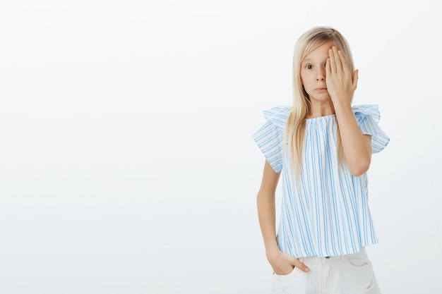 Jovem confusa, sentindo-se estranha ao ver algo vergonhoso. adorável filha fofa com cabelo claro, cobrindo um olho com a palma da mão