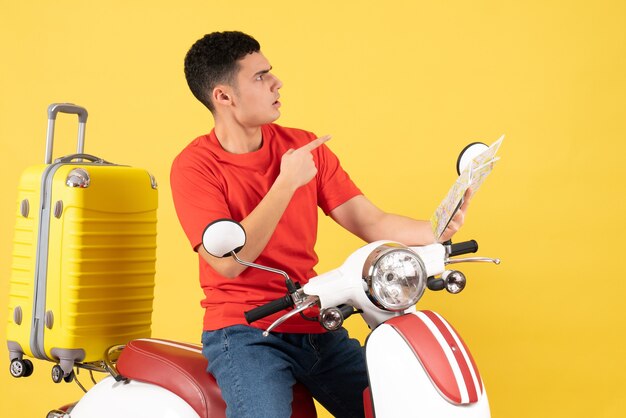 Jovem confuso de frente para um ciclomotor segurando um mapa olhando para algo