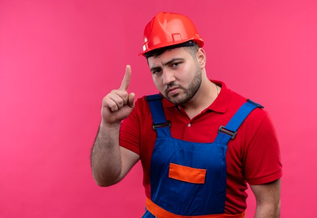Jovem construtor com uniforme de construção e capacete de segurança mostrando o dedo indicador