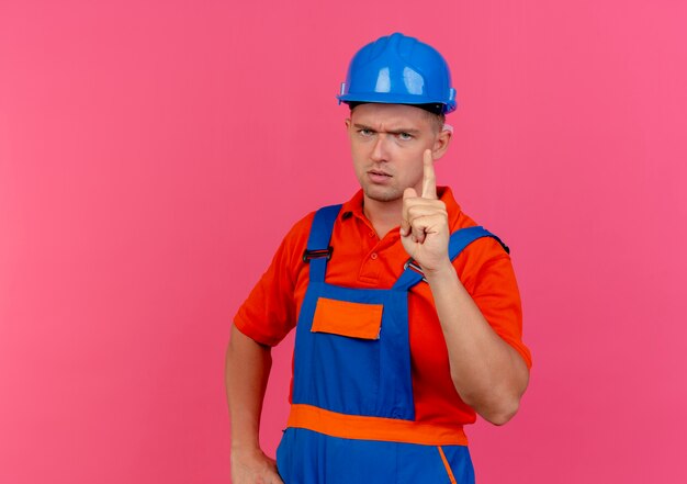 Jovem construtor rigoroso usando uniforme e capacete de segurança mostrando um em rosa