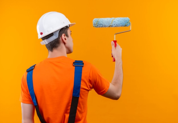 Jovem construtor usando uniforme de construção e capacete de segurança pinta a parede com uma escova giratória