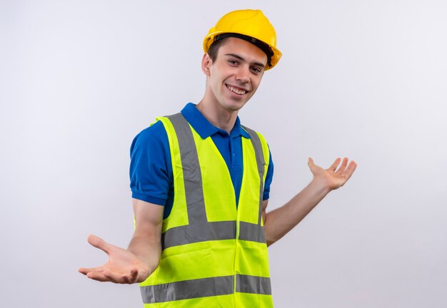 Jovem construtor vestindo uniforme de construção e capacete de segurança abre os braços e sorri