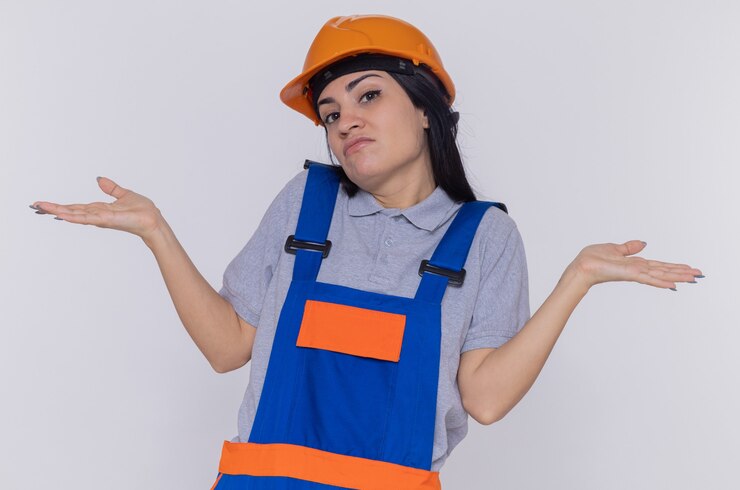 Foto grátis jovem construtora com uniforme de construção e capacete de segurança, olhando para a frente, confusa, encolhendo os ombros e encolhendo os ombros em pé sobre a parede branca