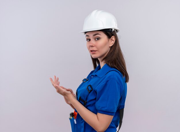 Jovem construtora confiante com capacete de segurança branco e uniforme azul fica de lado e bate palmas no fundo branco isolado com espaço de cópia