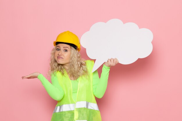 Jovem construtora feminina em construção verde com capacete amarelo segurando uma grande placa branca no espaço rosa trabalho arquitetura construção