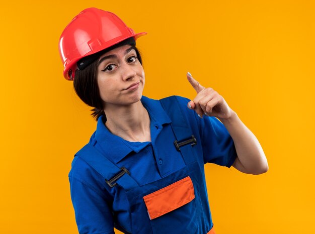 Jovem construtora impressionada de uniforme aponta para a câmera