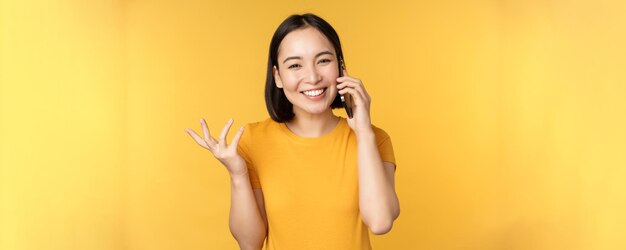 Jovem coreana falando no celular mulher asiática ligando para smartphone em cima de amarelo bac