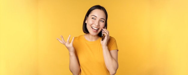 Jovem coreana falando no celular Mulher asiática ligando para smartphone em pé sobre fundo amarelo