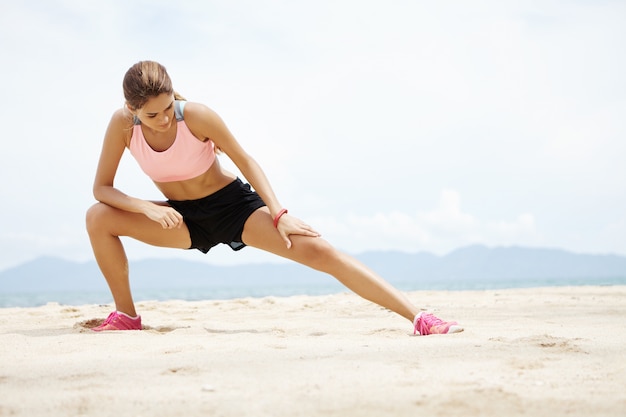 Jovem corredor feminino com belo corpo em forma, aquecendo os músculos antes do treino cardiovascular de treinamento de força.