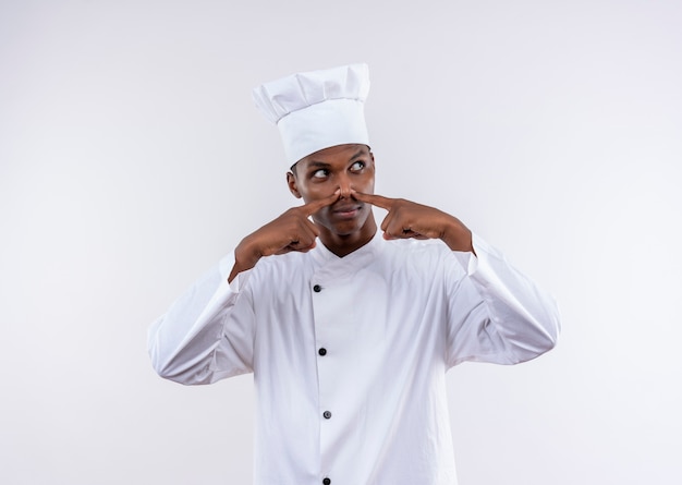 Jovem cozinheira afro-americana irritada com uniforme de chef fecha nariz isolado no fundo branco com espaço de cópia