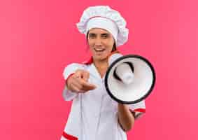 Foto grátis jovem cozinheira alegre vestindo uniforme de chef segurando um alto-falante, mostrando seu gesto na parede rosa isolada com espaço de cópia