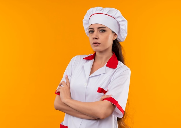 Jovem cozinheira caucasiana confiante com uniforme de chef cruzando os braços isolados na parede laranja com espaço de cópia