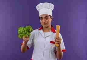 Foto grátis jovem cozinheira caucasiana confiante em uniforme de chef com salada e molho de espaguete isolado na parede violeta com espaço de cópia